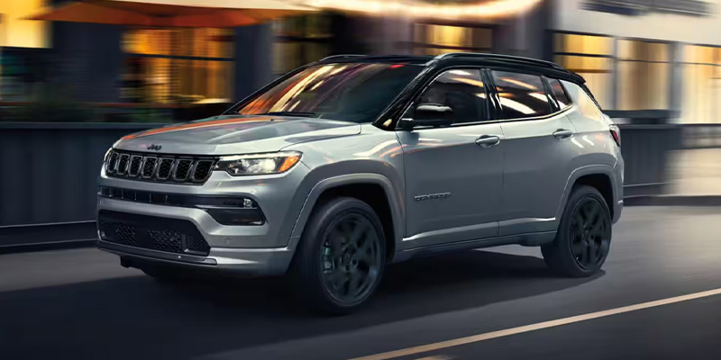 A silver 2026 Jeep Compass SUV seen from the front and driver's side drive down a street in Medina, OH
