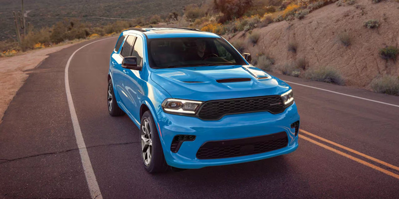 A blue 2026 Dodge Durango driving on a winding road through a desert landscape.