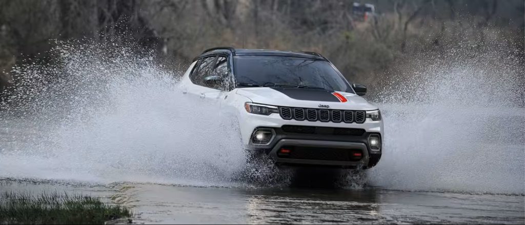 White Jeep SUV driving through water splash outdoors.