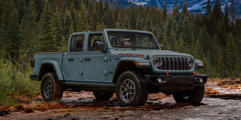 Gray Jeep Gladiator Rubicon pickup truck driving through a forest trail.