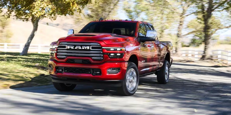 Red RAM heavy-duty pickup truck driving along a tree-lined road.